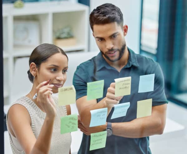 Um homem e uma mulher olhando para notas adesivas em uma parede de vidro. Parceiros de negócios em uma agência de marketing digital.